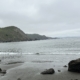 Ocean with rocks near and cliffs far. Grey sky